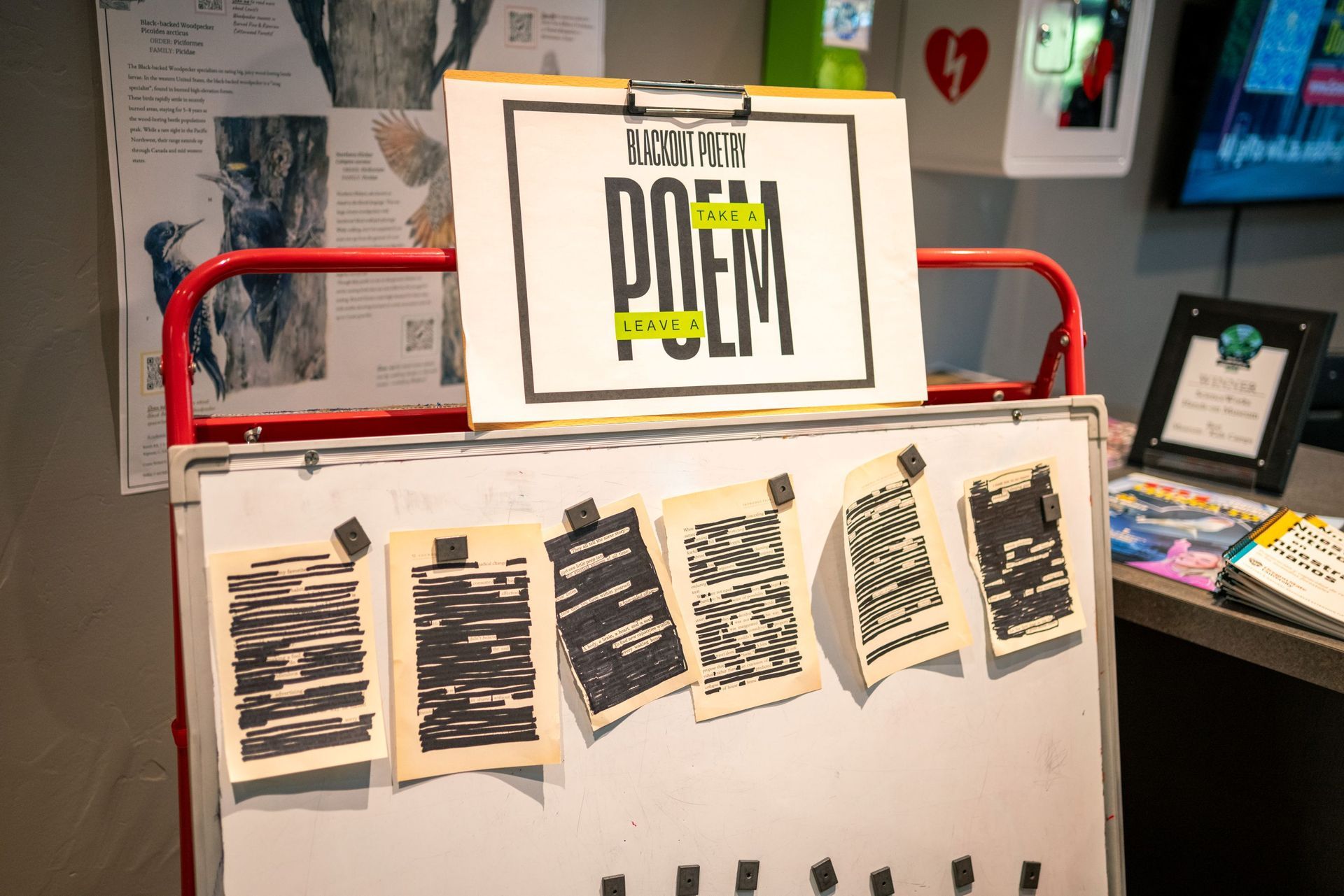 Display board with “take a poem, leave a poem” sign and several torn paper notes clipped across the front.