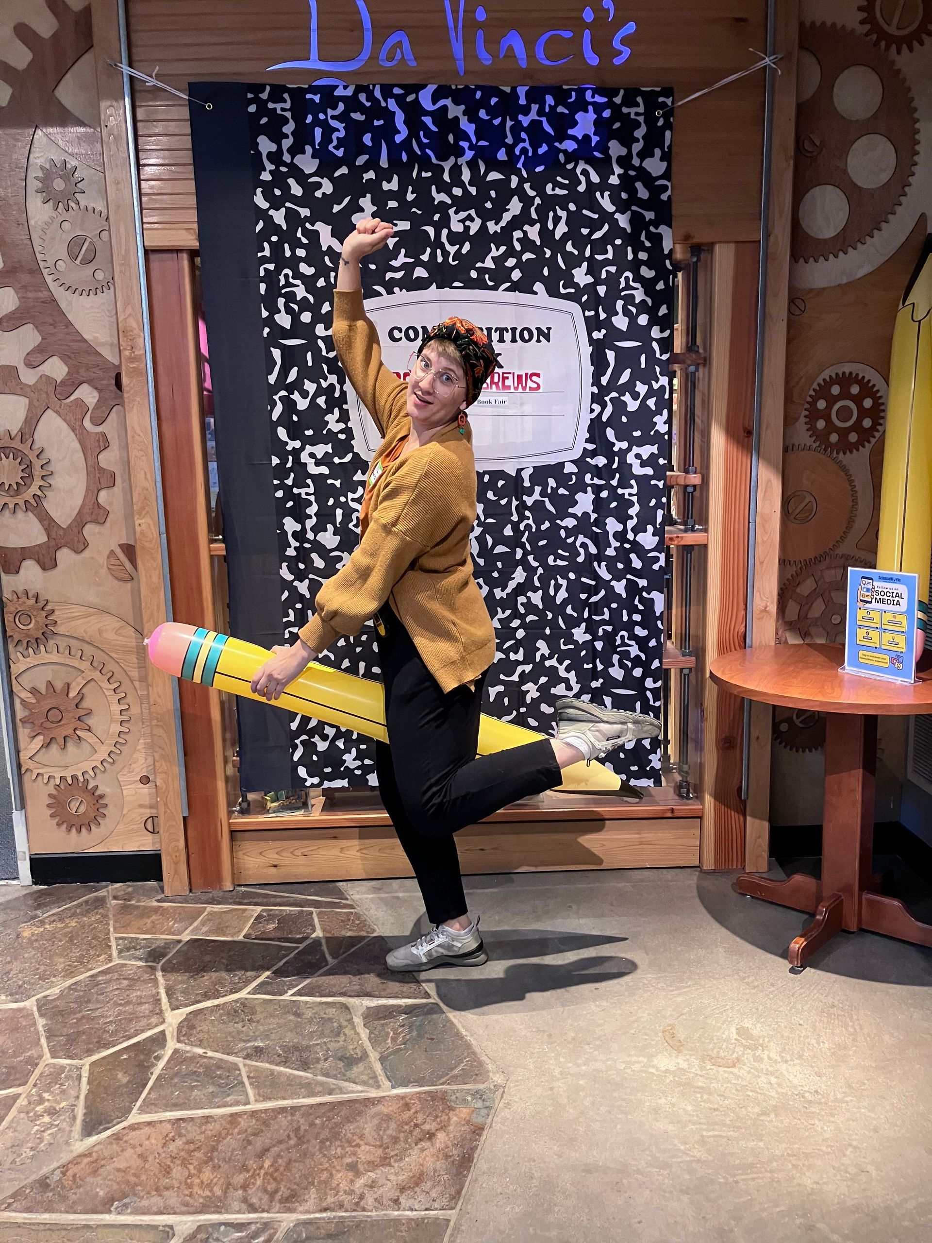Person posing playfully in front of a patterned backdrop with a raised arm and colorful outfit