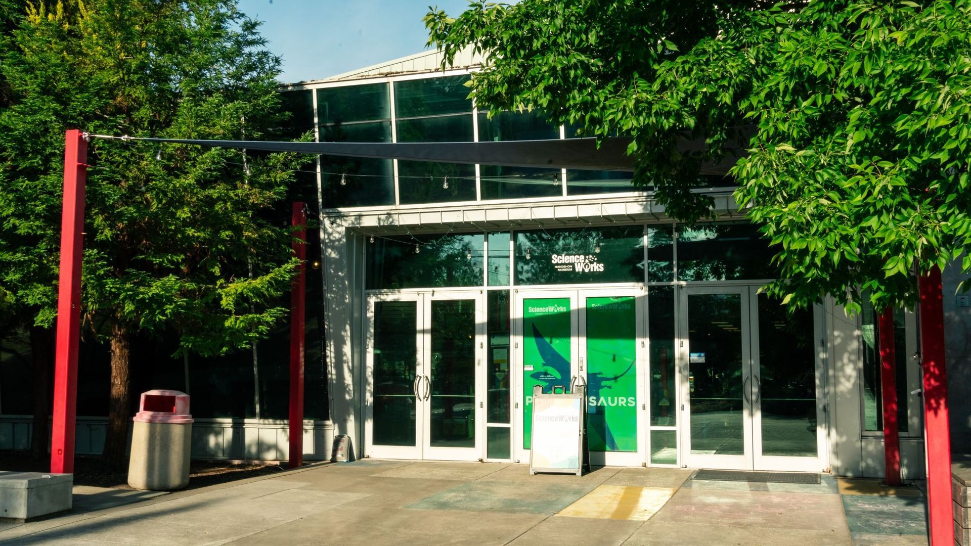 ScienceWroks Building entrance, Glass doors,  red posts, and trees on both sides