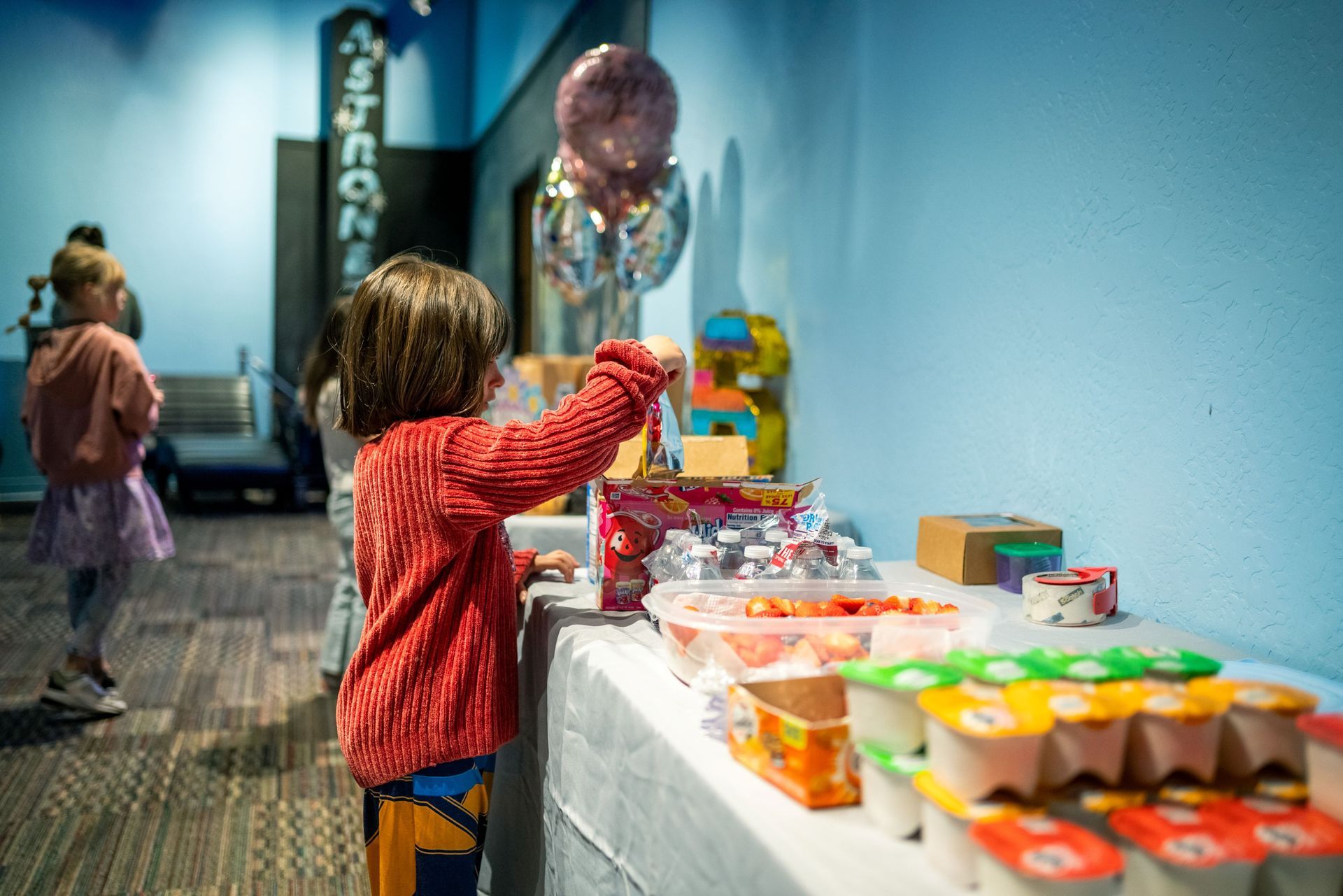 Child reaching toward balloon with colorful treats on a white table indoors