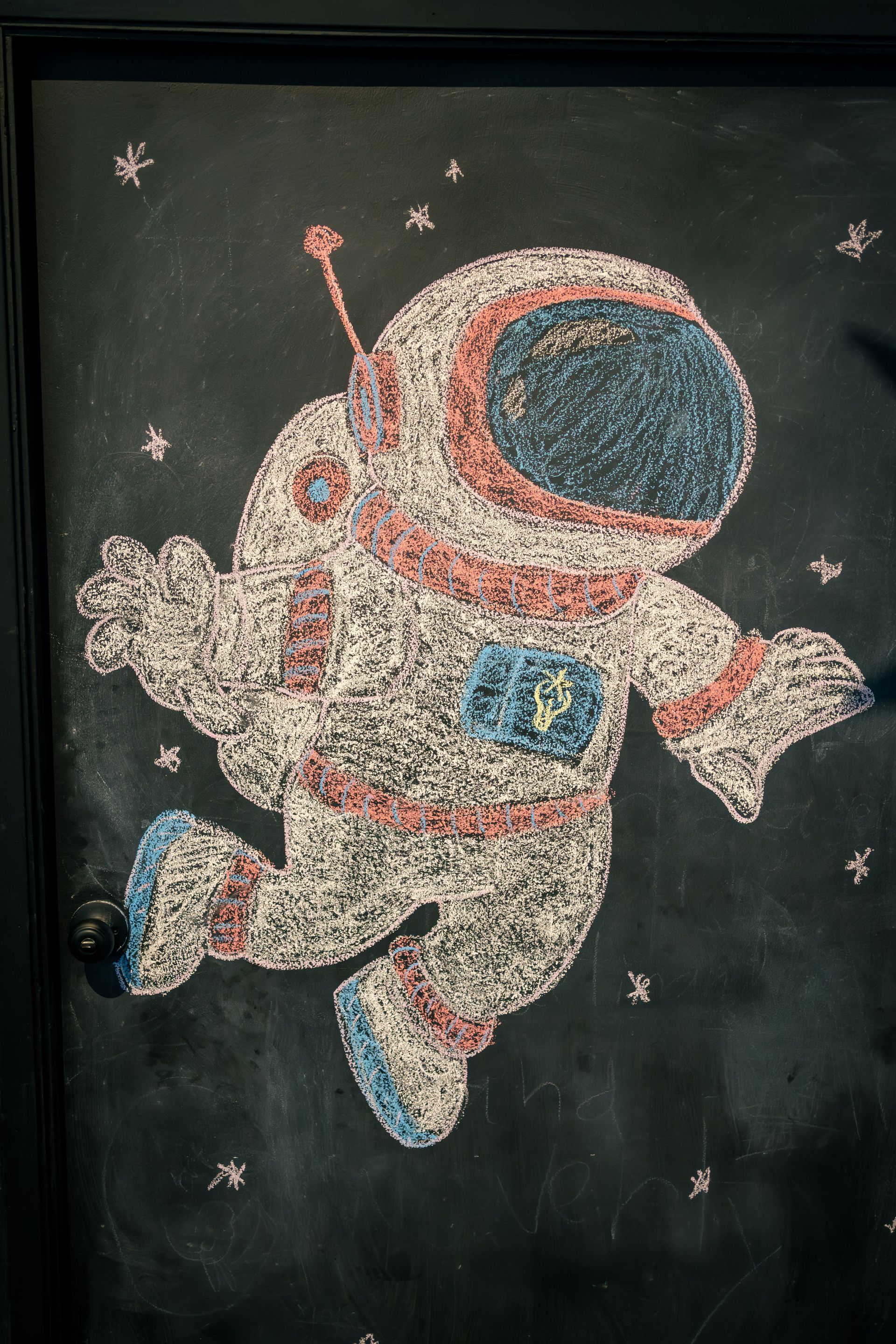 Chalk drawing of an Astronaut floating on a black chalkboard background with stars