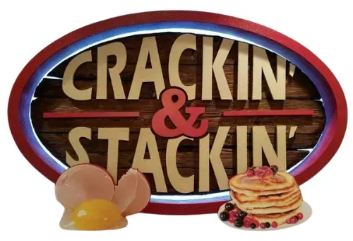 Crackin’ & Stackin’ sign with pancakes, eggs, bacon, and berries on a red oval background