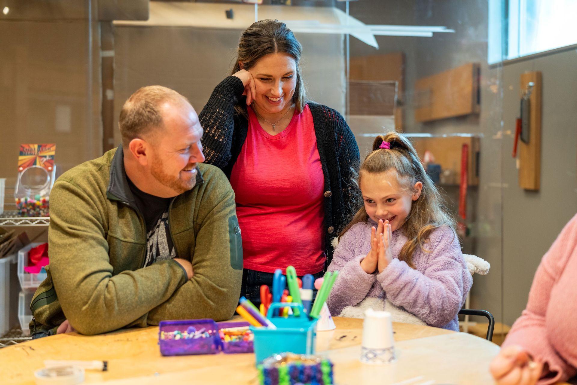Family gathered around a table, smiling and chatting with craft supplies in a bright indoor room