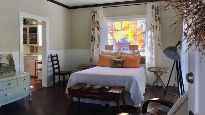 Cozy bedroom with a white bed, colorful window, dresser, chair, and a floor lamp.