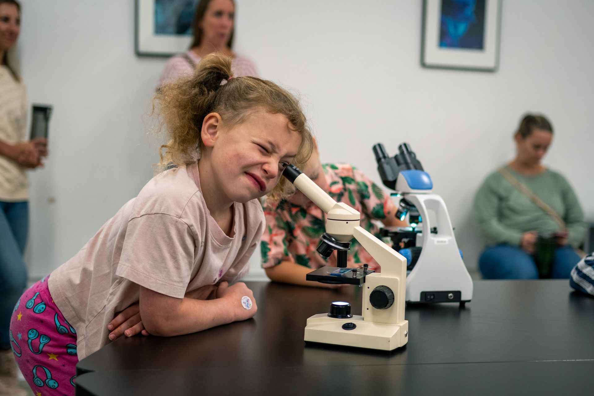 Child peering into a microscope at a museum table with others watching in the background