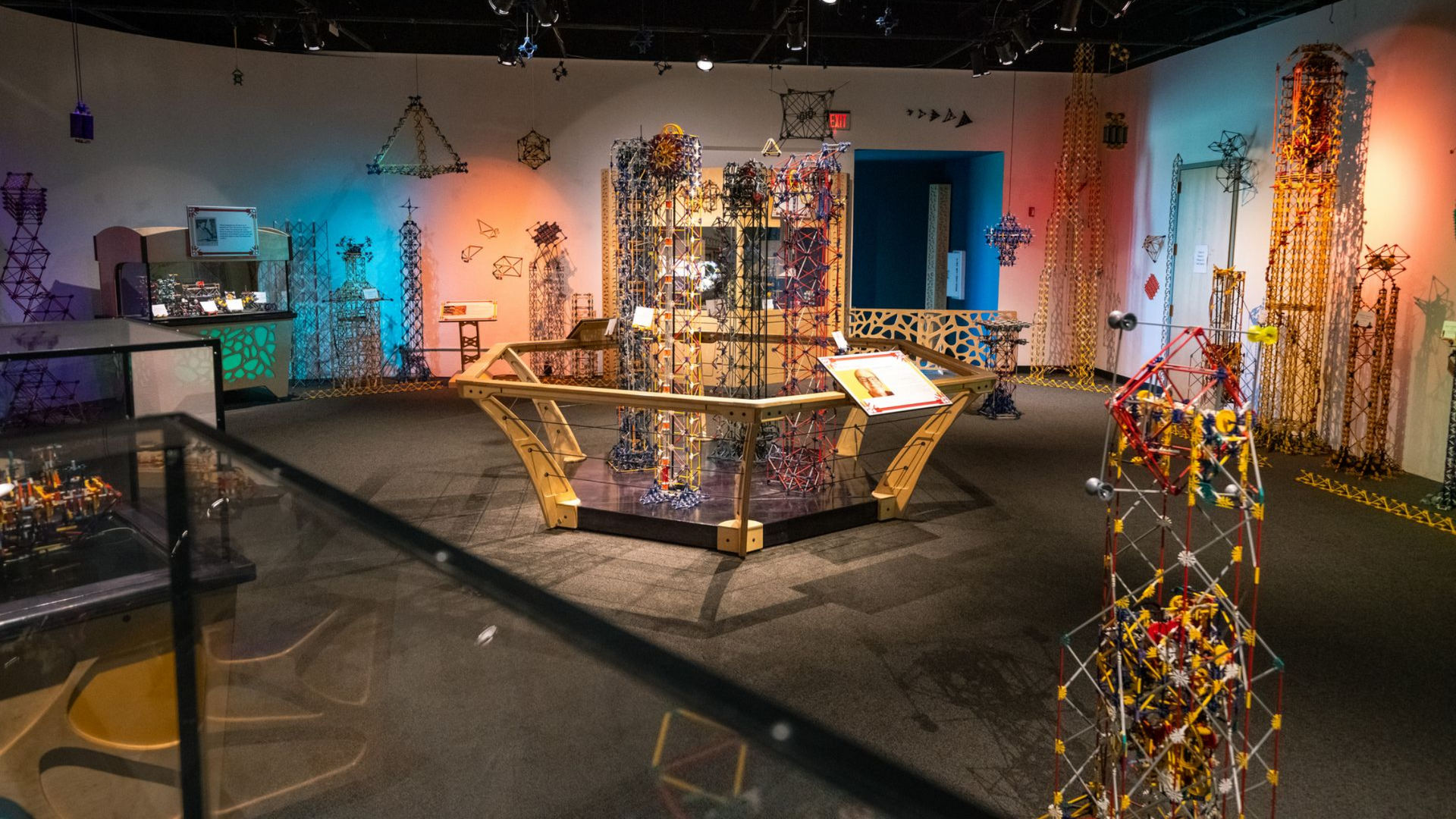 Colorful art installation in a gallery with glowing lights, hanging sculptures, and central display platforms