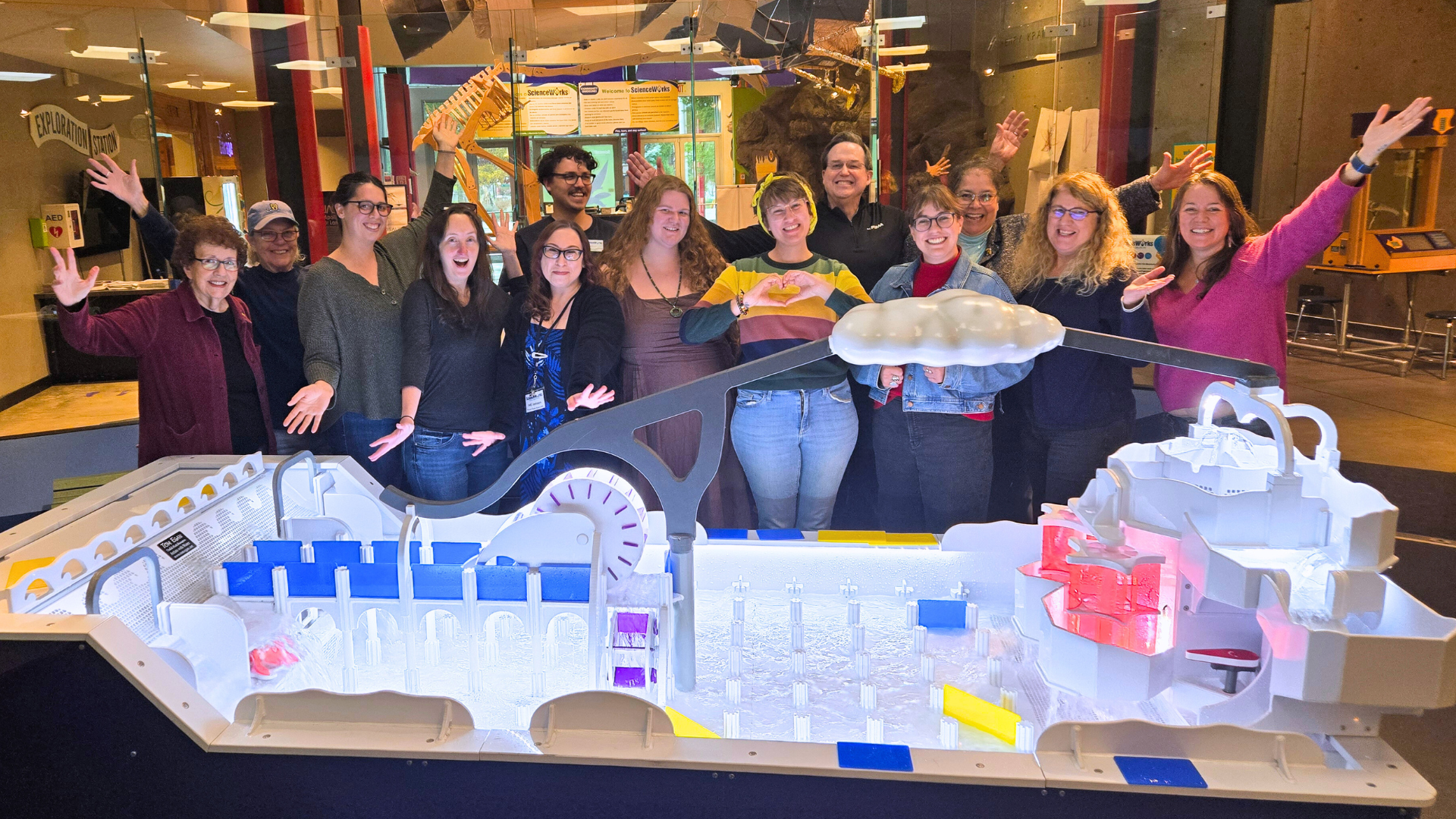 ScienceWorks staff pose with new water table exhibit. They are smiling and have their arms raised.