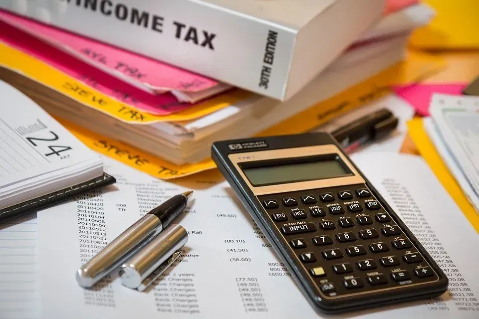Tax documents, calculator, pen, and folders on a desk; financial paperwork.