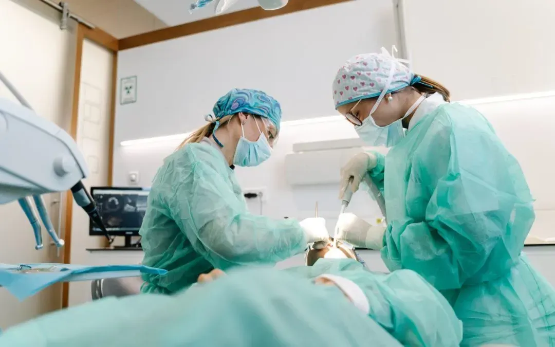 Two dental professionals in scrubs perform a procedure on a patient in a dental office.