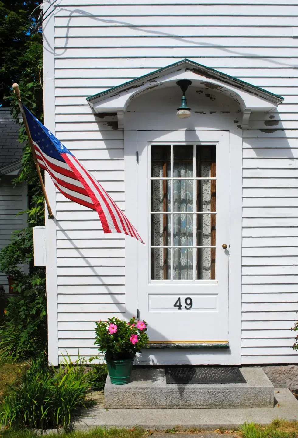 White building entrance with American flag, door with number 49, pink flowers.
