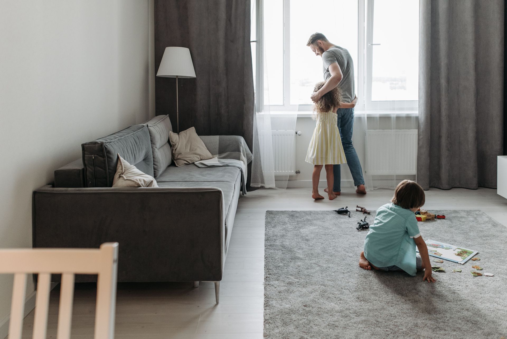 Father and daughter looking out window, while son plays with a puzzle