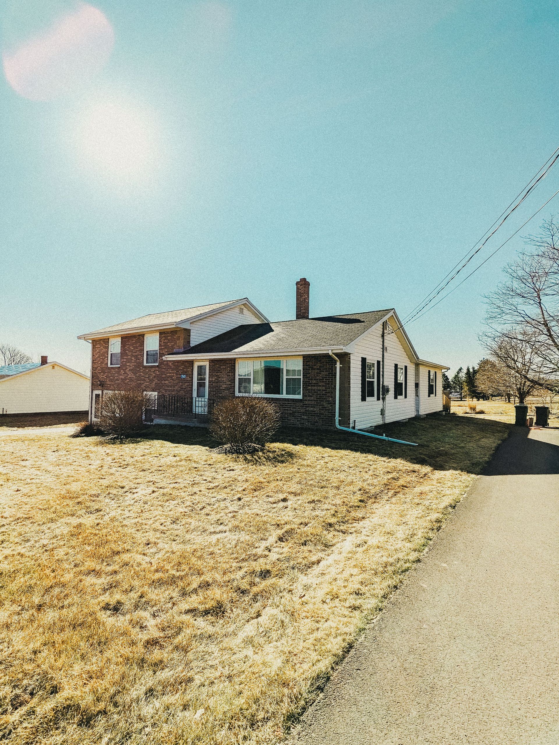 A home with a grass lawn in the front and the sun shining above it.