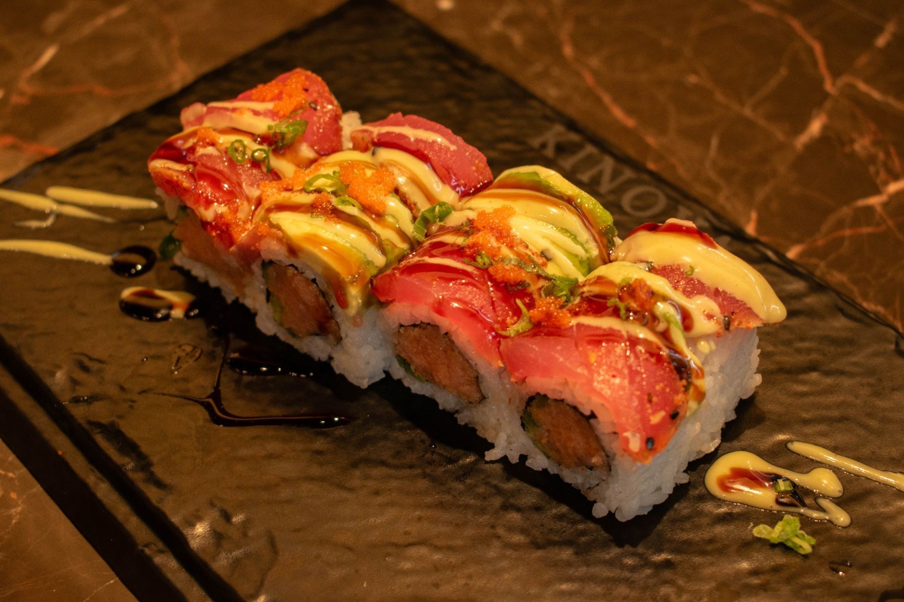 Sushi rolls drizzled with sauce and colorful toppings on a dark stone plate