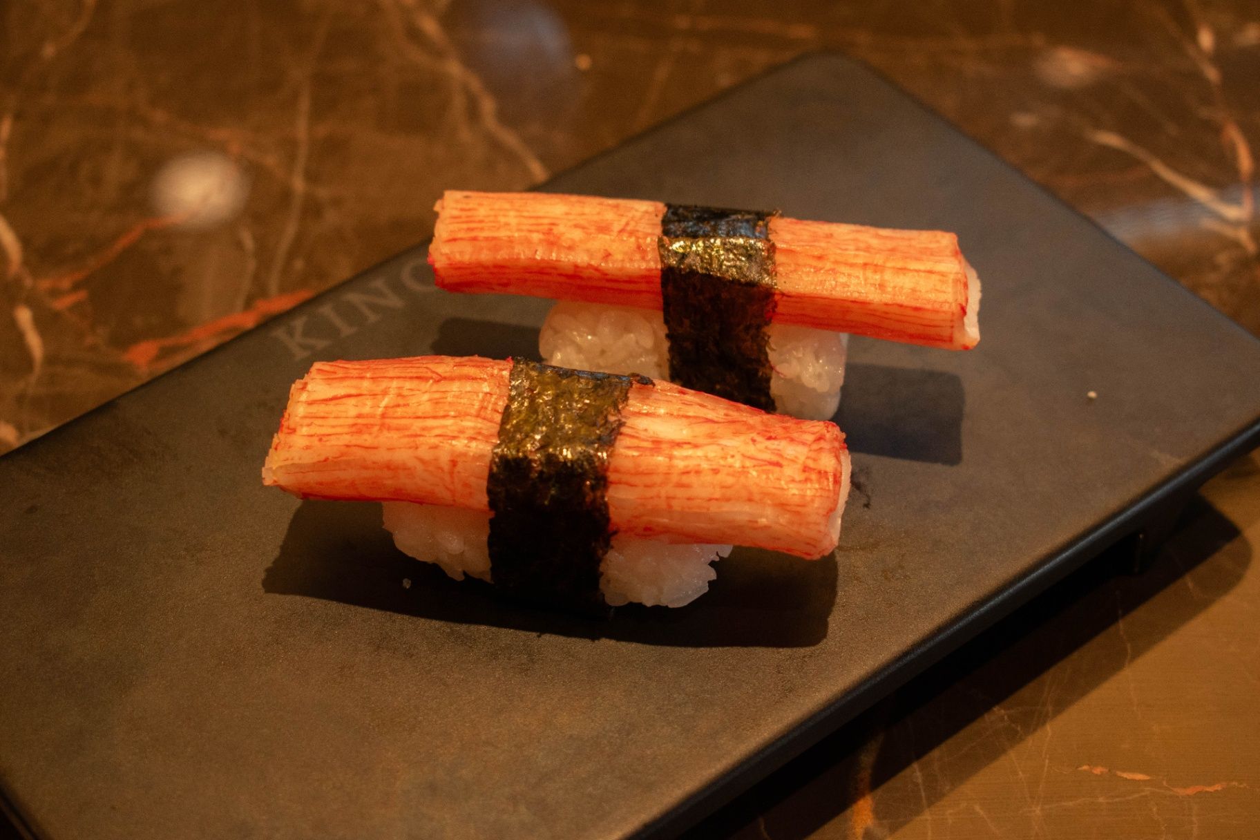 Two crab sushi nigiri on a black plate, topped with black seaweed bands