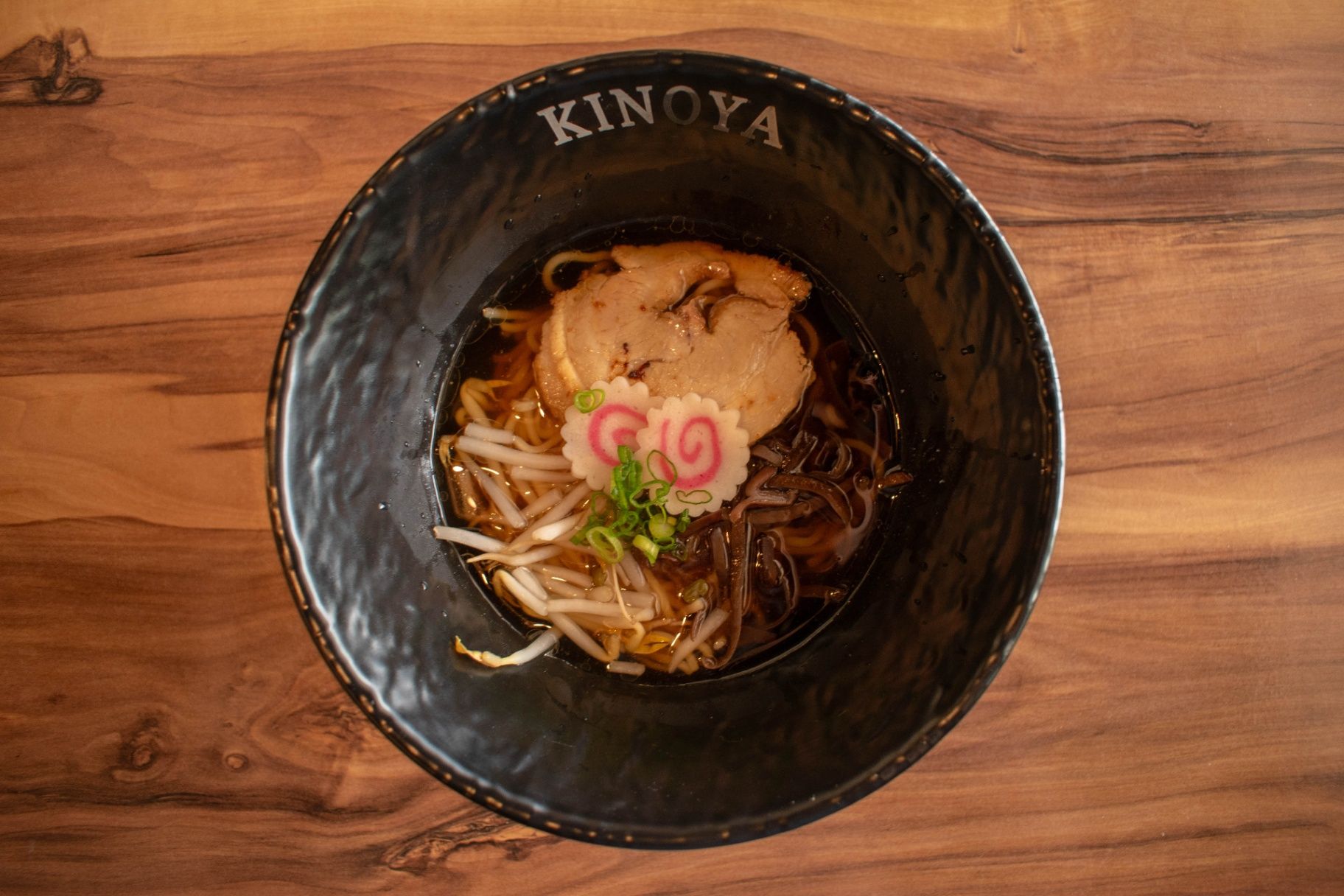 Black bowl of ramen with toppings on a wooden table, viewed from above