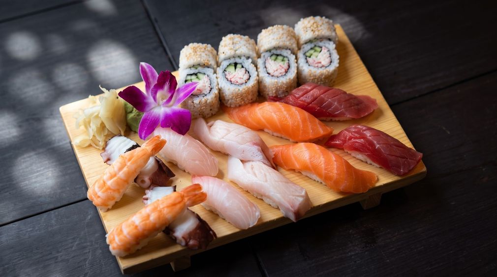 Assorted sushi rolls and nigiri on a wooden platter with a purple orchid garnish