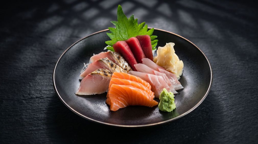 Sushi platter with salmon, tuna, and garnishes on a dark plate