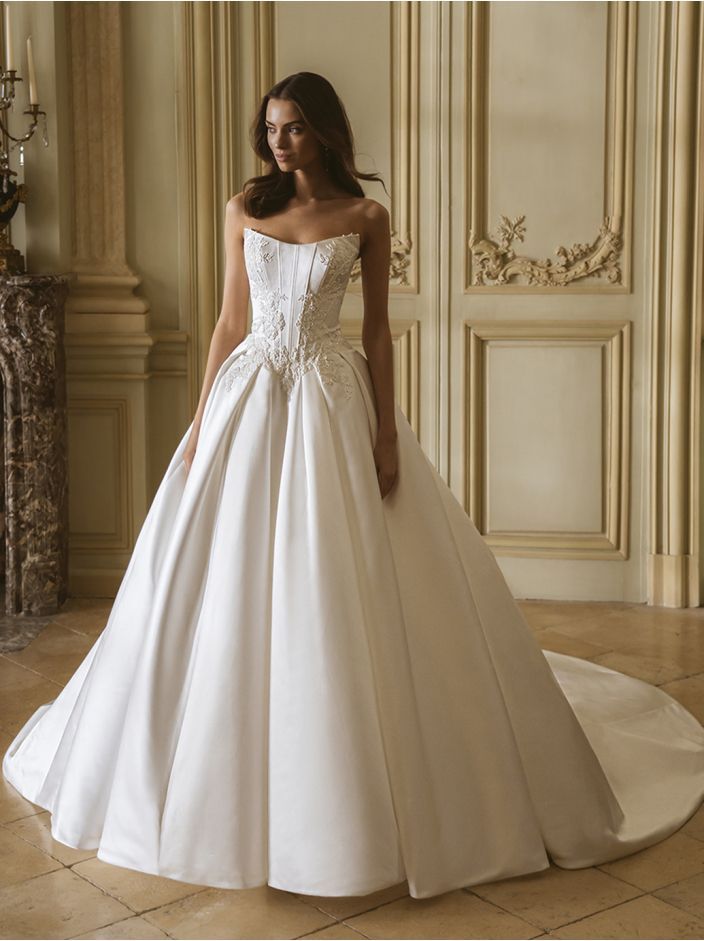 Woman in a long, white wedding dress with lace detail on the side and a train, posing in a studio.