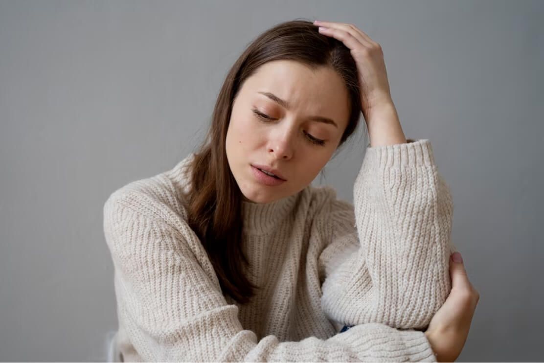 A woman in a sweater is holding her head.