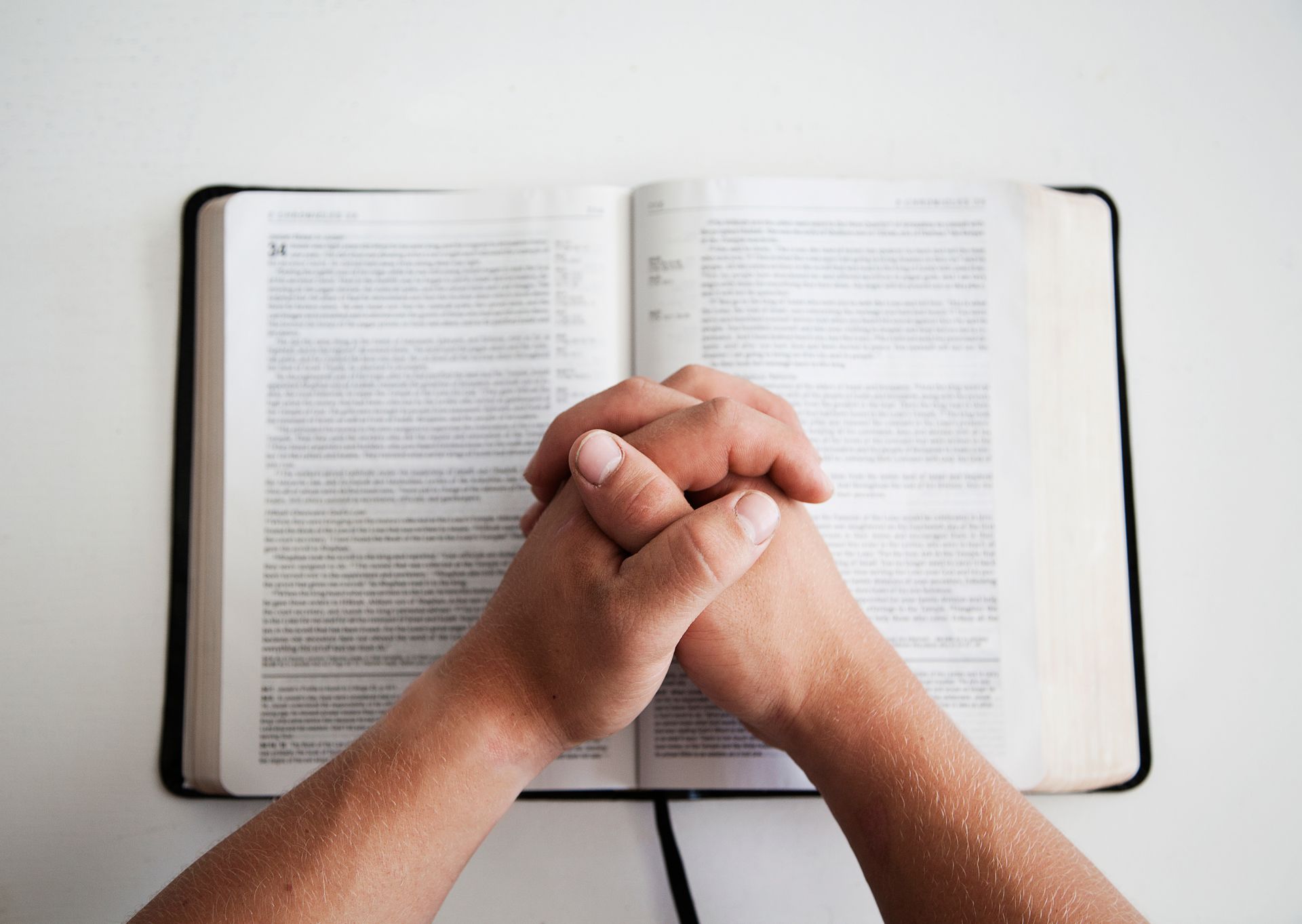A person is holding a rosary in their hands over an open bible.