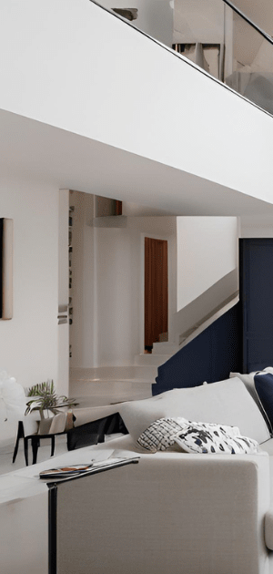 Modern living room with white walls, a gray sofa, navy pillows, and an open loft overlooking a staircase