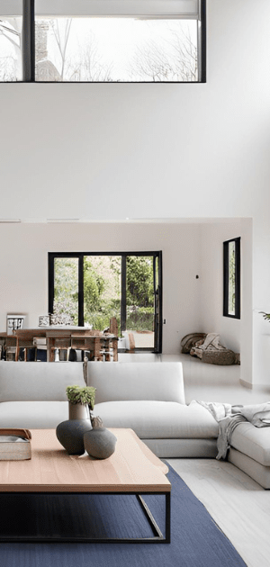 Bright modern living room with white sectional sofa, black window frames, and light wood coffee table.