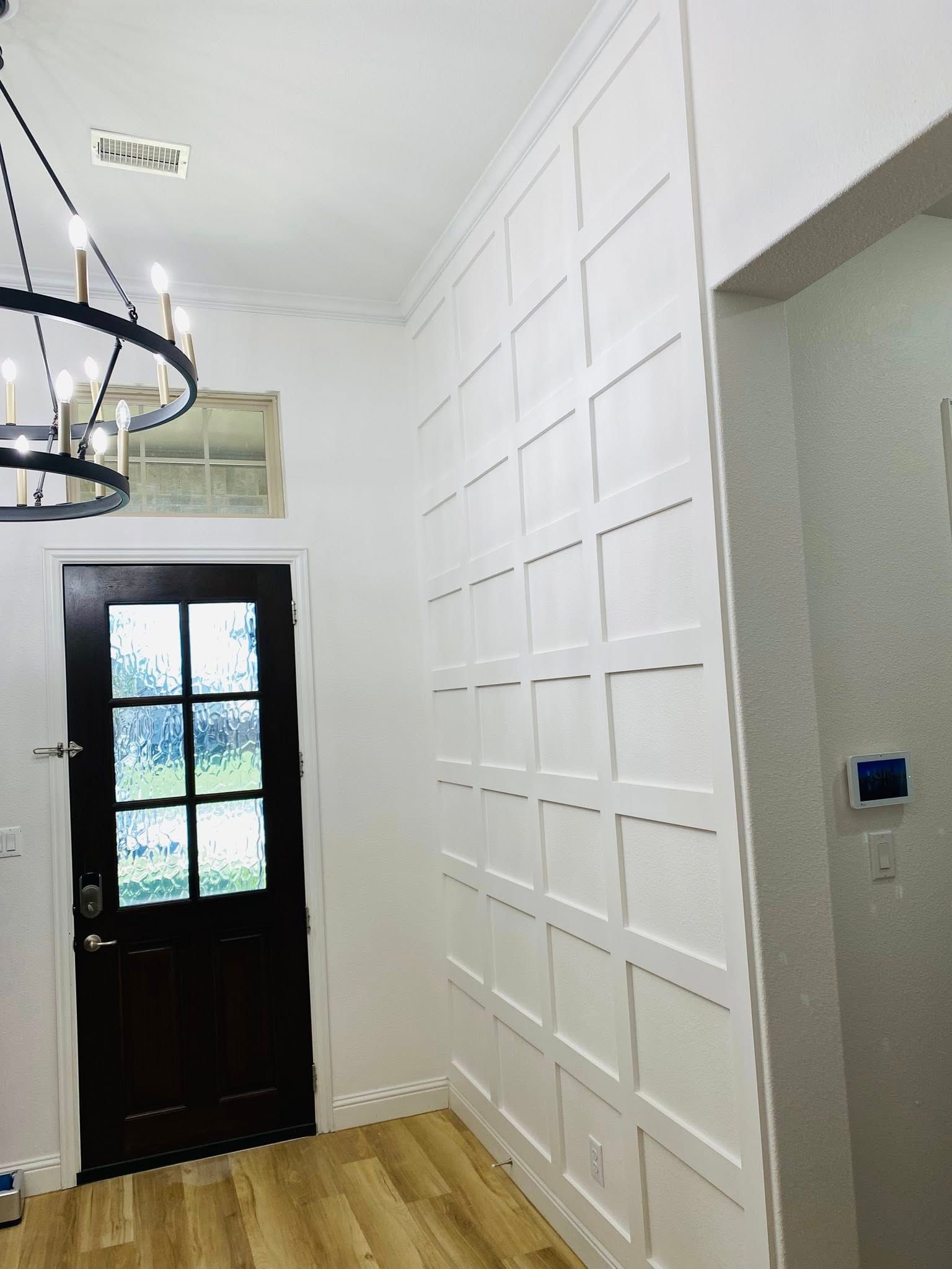 White paneled accent wall in entryway with a dark door and chandelier.