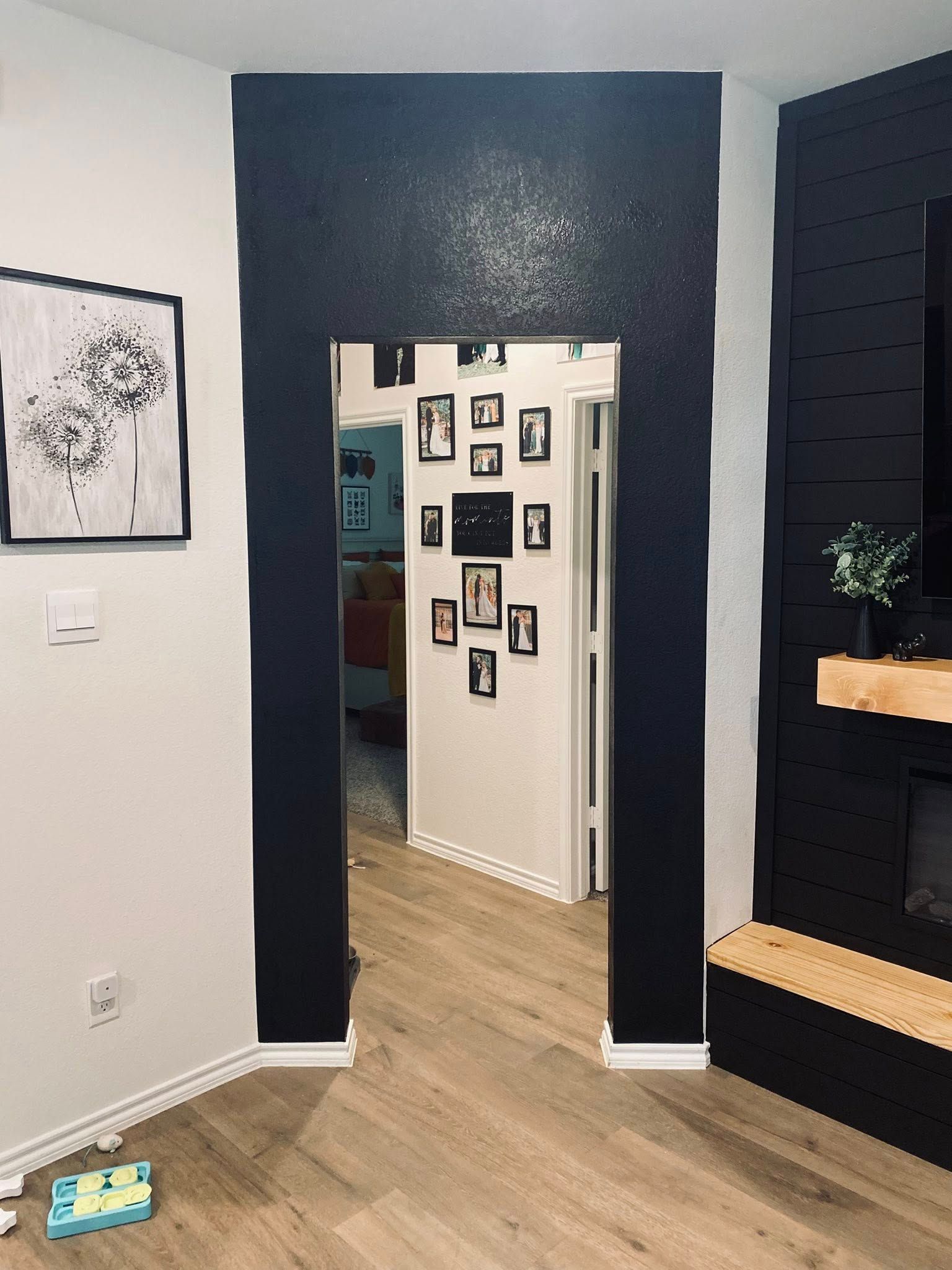 Black wall framing an open doorway; interior with wood floors, white walls, art, and fireplace.