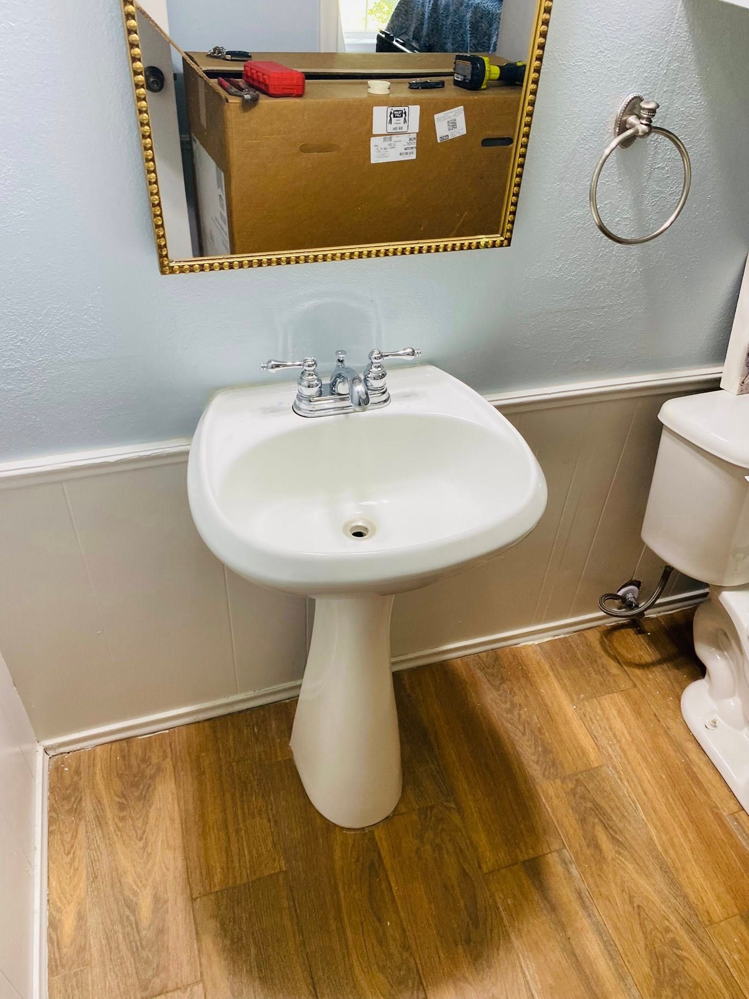 White pedestal sink in bathroom with mirror, toilet, and towel ring.