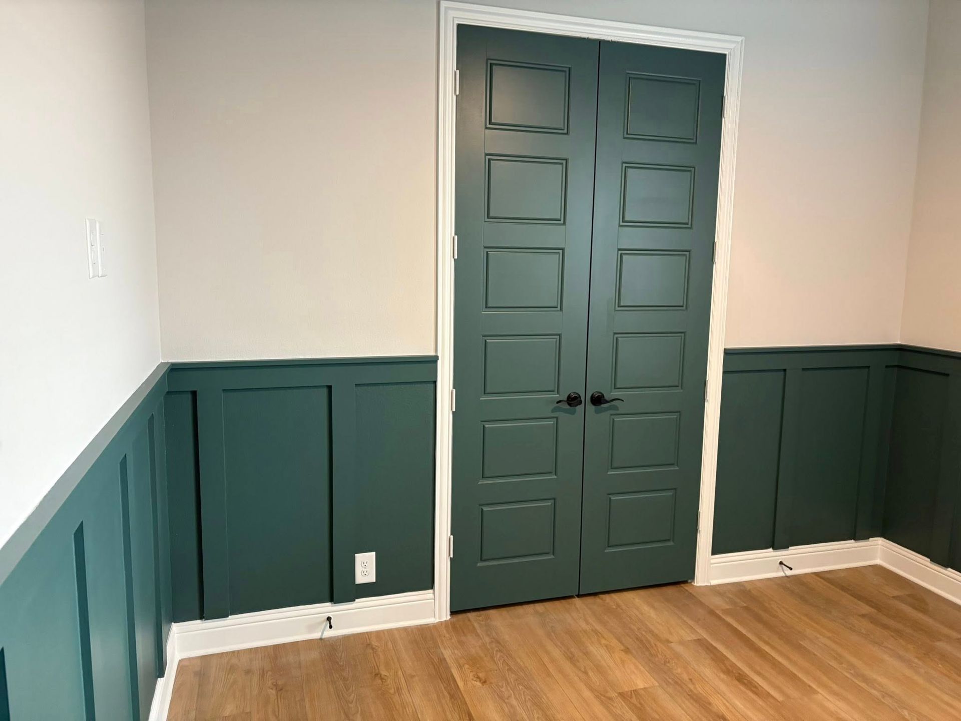 Green paneled walls and matching doors in a room with light wood floors and white walls.