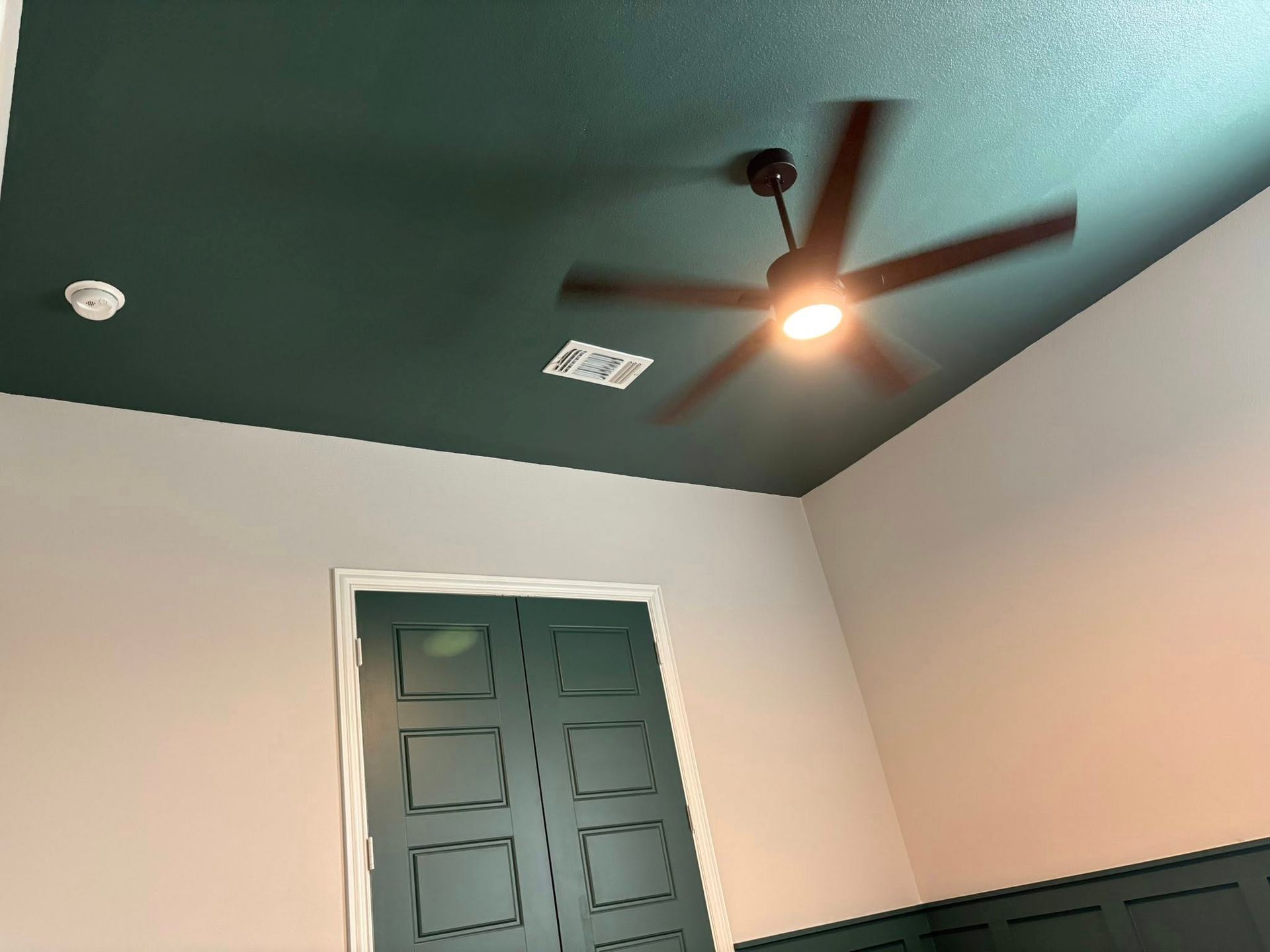 Dark green ceiling with ceiling fan, white walls, green door.