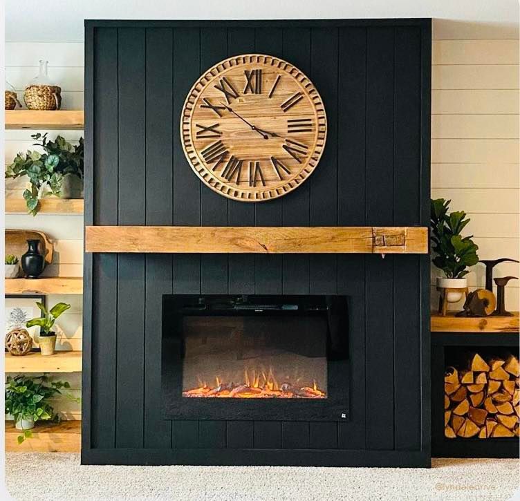 Black fireplace with wooden mantel, electric fire, and clock. Wooden shelves on either side, plants.