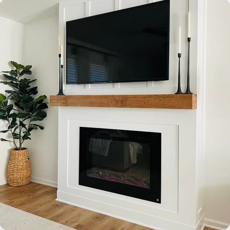 Modern white fireplace with a mounted TV, wood mantel, and tall candles.