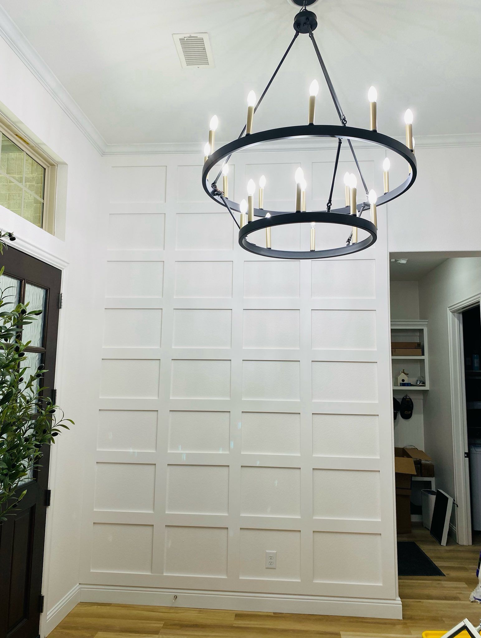 White paneled wall with a black chandelier, entry with a dark door, and wood-look flooring.