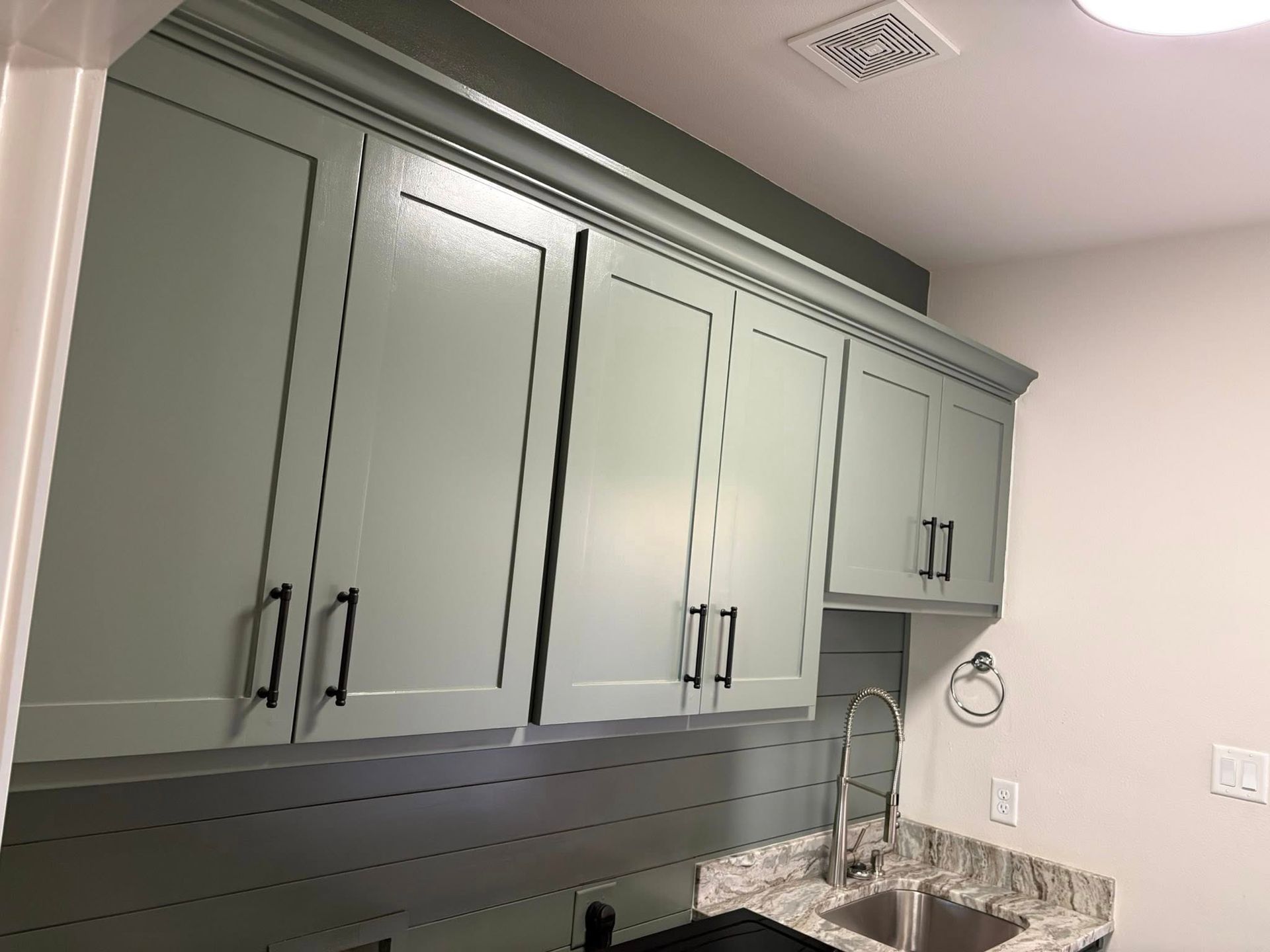 Green kitchen cabinets with black handles, above a sink and countertop.