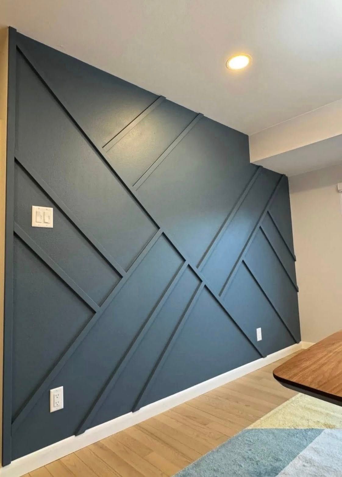 Blue geometric wall paneling with electrical outlets, above wood floor, corner.