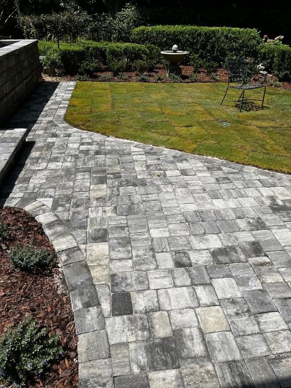 Stone paved patio next to a grassy yard. Curving walkway with planted garden beds.