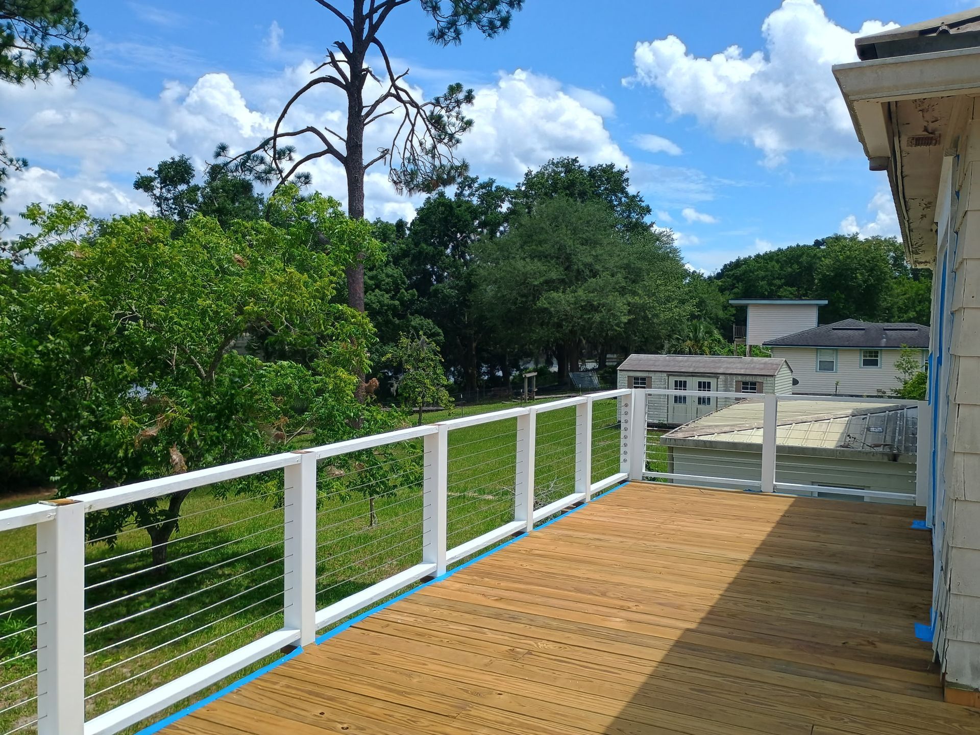 Wooden deck with white railing, overlooking trees and a blue sky.