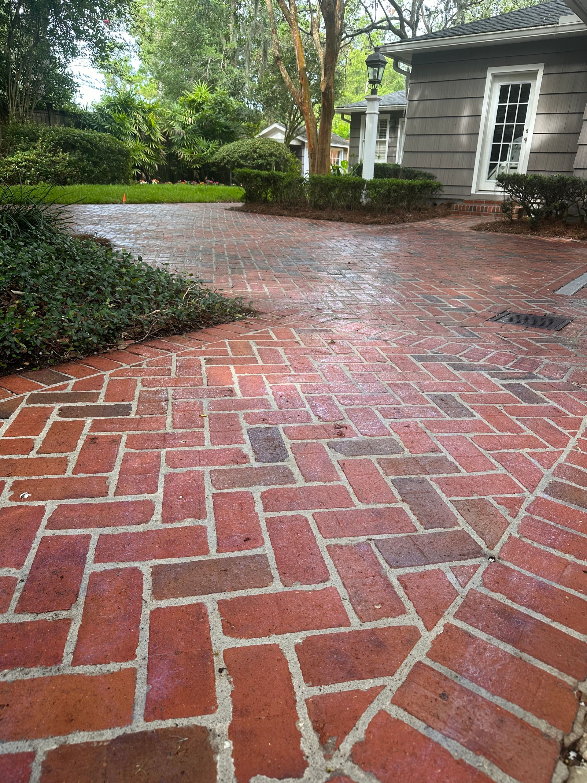 Red brick patio in a herringbone pattern with surrounding greenery and a gray building.