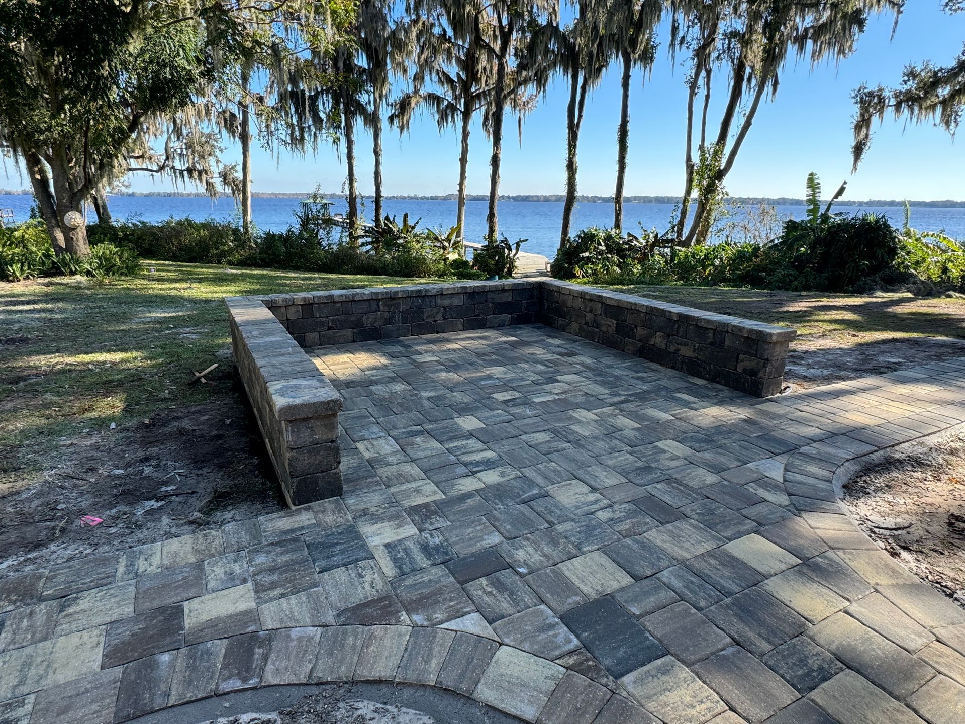 Brick patio with low retaining walls near water and trees.