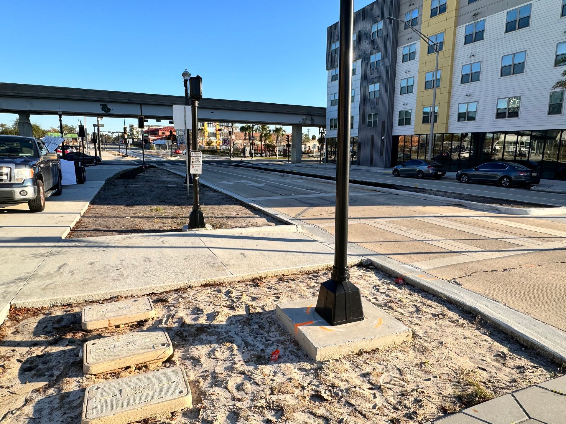 Sidewalk with street, new construction building. Concrete and brick pavers, sandy areas.