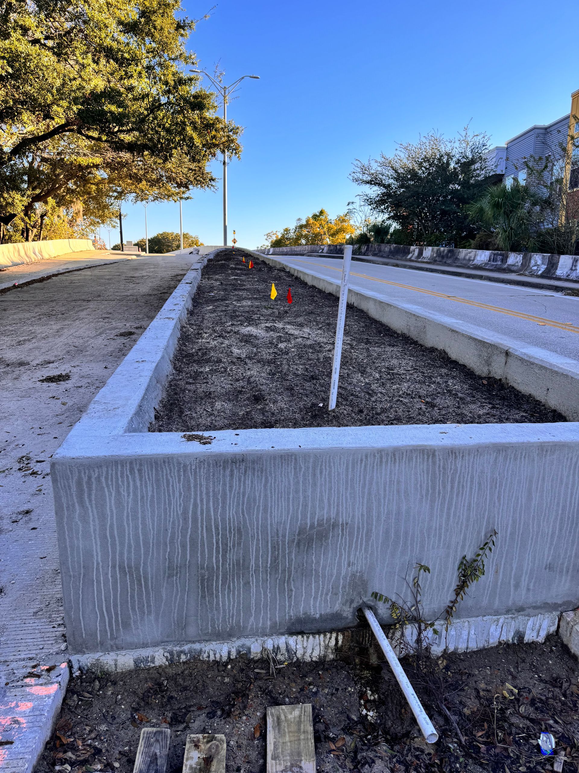 Concrete planter box next to a road, filled with soil and marked with flags.