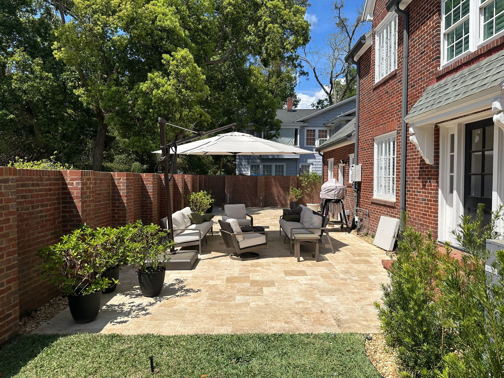 Backyard patio with brick wall and seating area, umbrella, and grill. Sunny day.