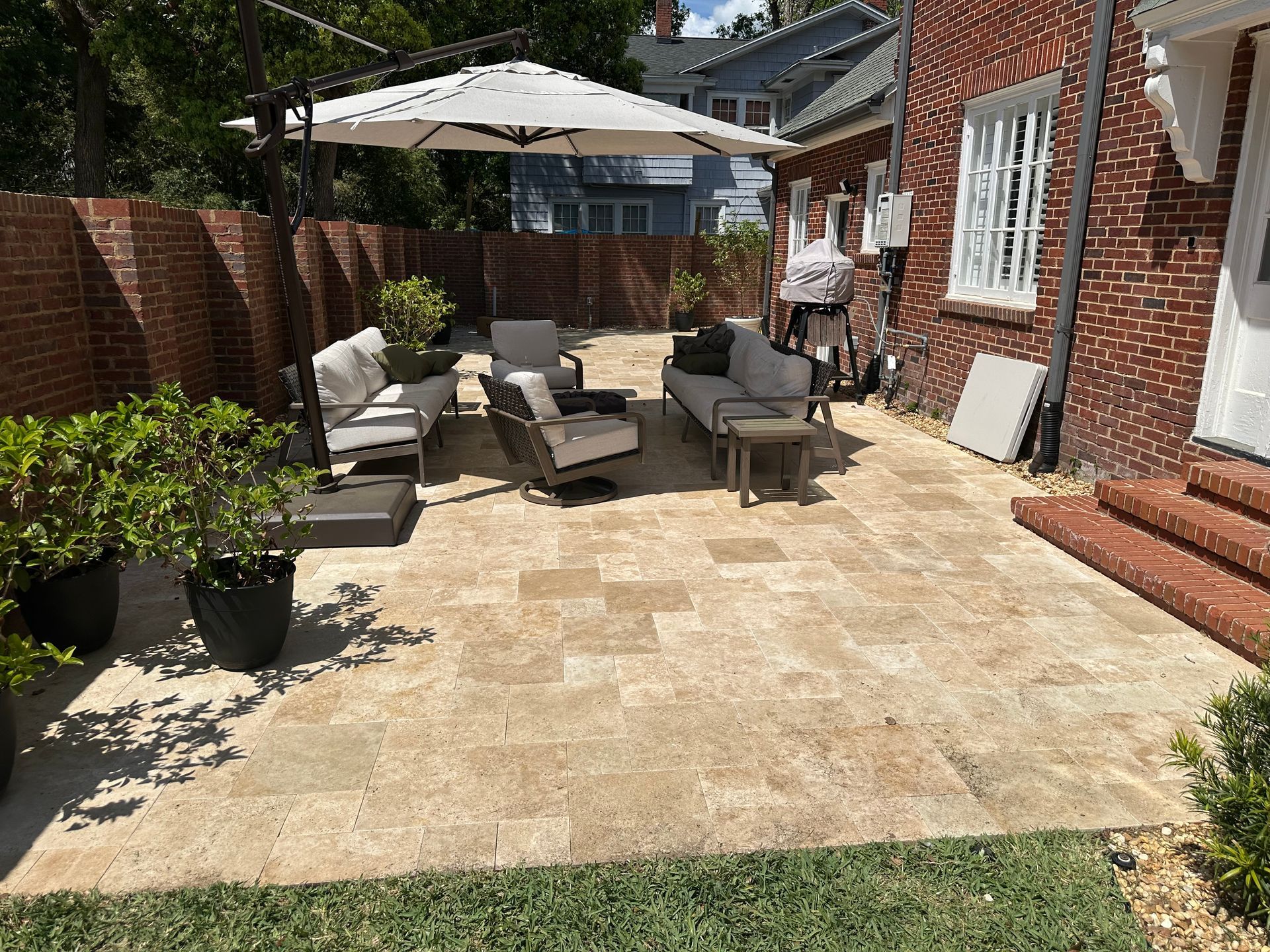 Patio with beige pavers, outdoor furniture, brick walls, and a large umbrella.