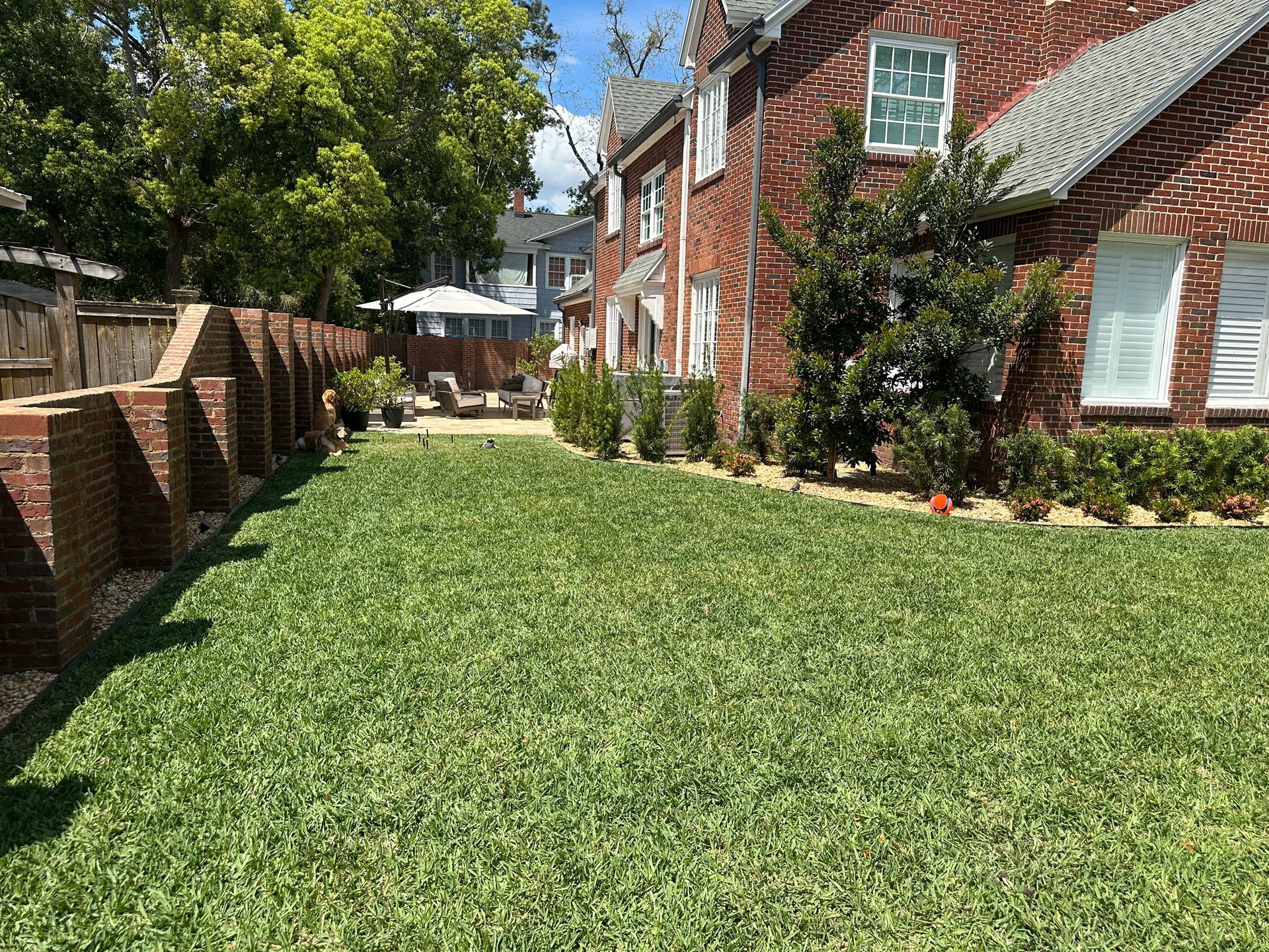 Green lawn with brick wall and red brick house.