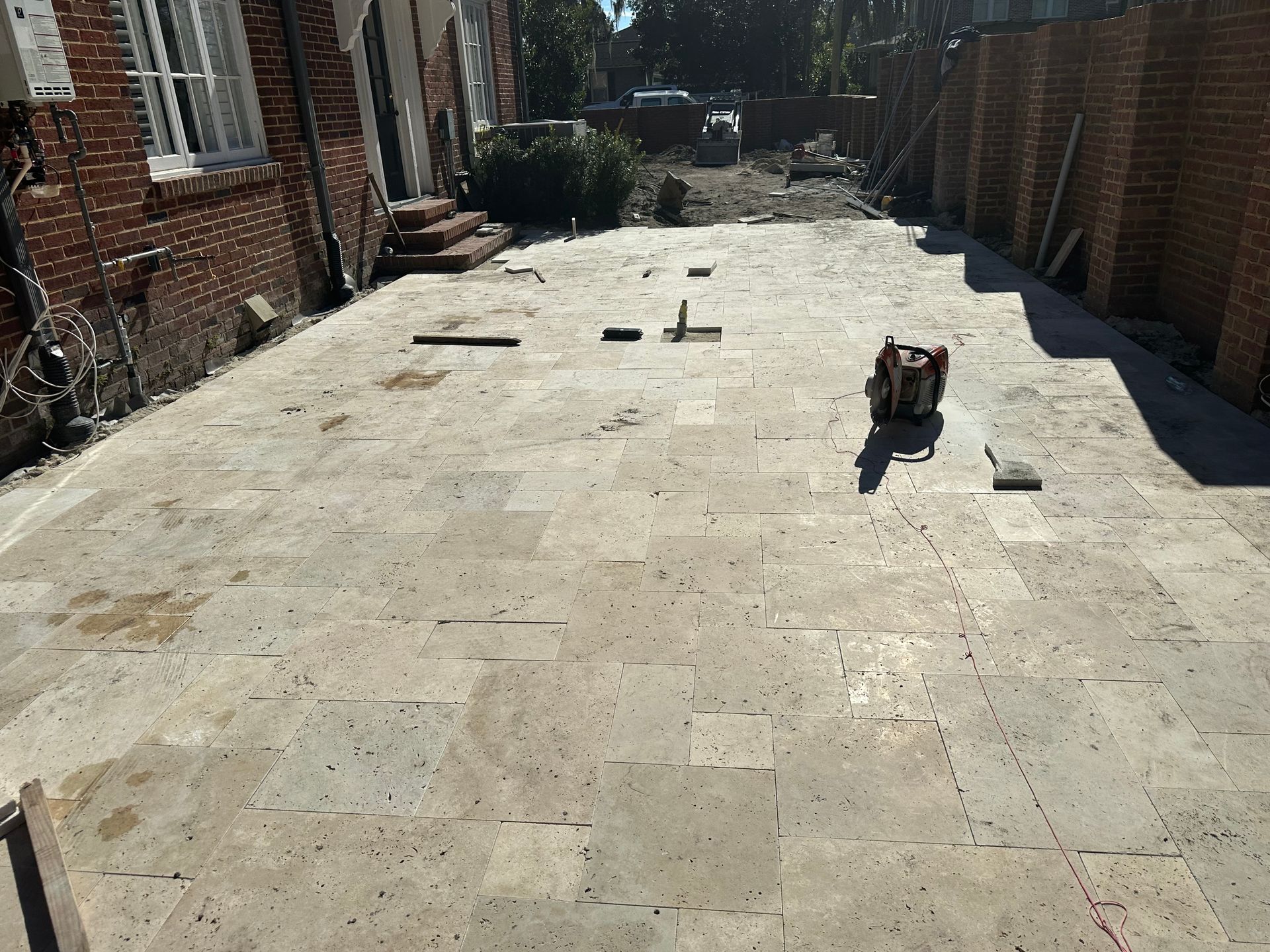 Stone patio with bricks, tools, and a building on either side.