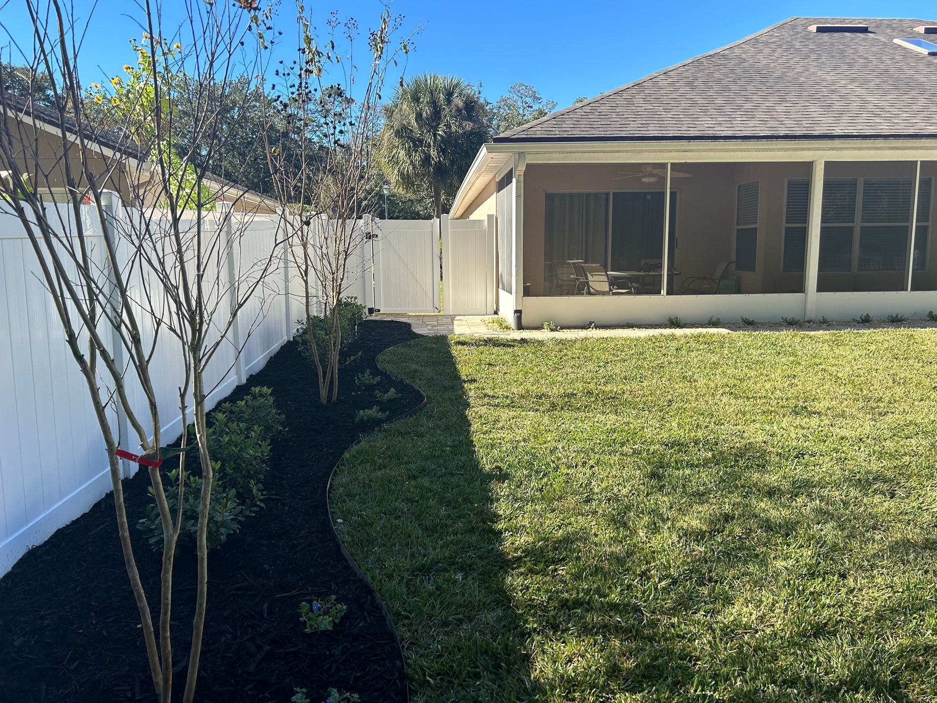 Backyard with white fence, landscaping with mulch and bushes, and screened porch.