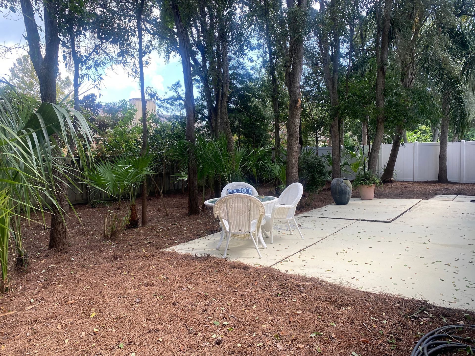 Backyard with a patio, white chairs, trees, and mulch ground covering.