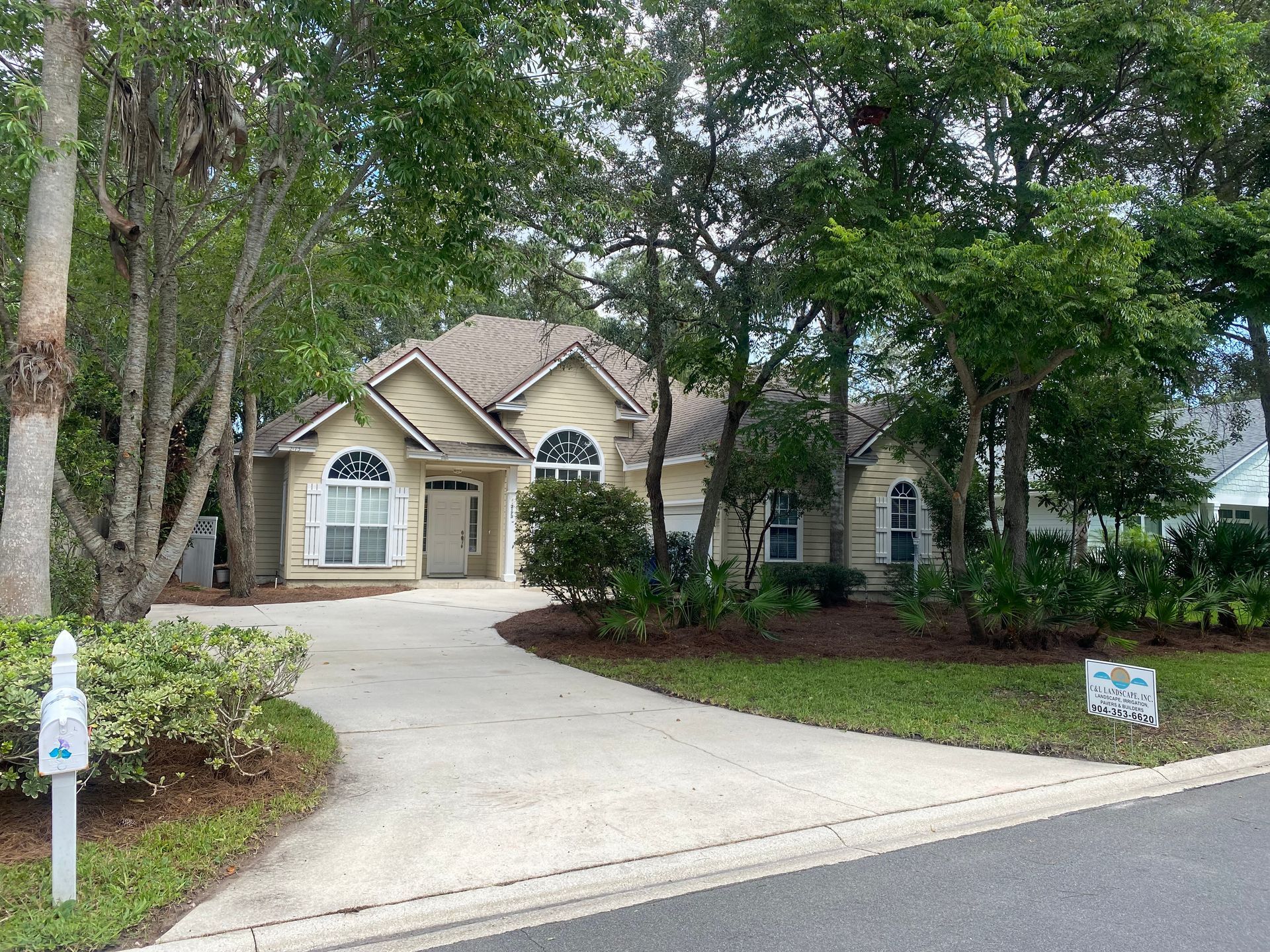 Beige house with arched windows and driveway. Surrounded by trees and landscaping.