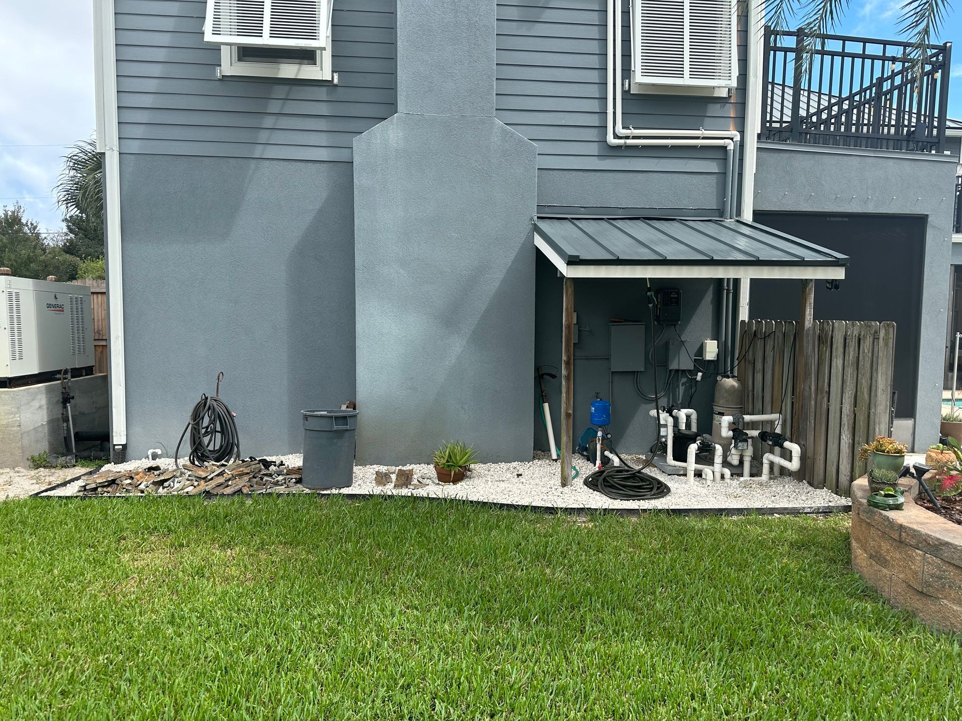 Backyard with a gray house and chimney, pool equipment under a shed roof, and a green lawn.